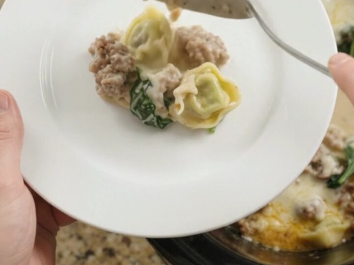 Creamy slow cooker tortellini with sausage and mushrooms in a black crockpot