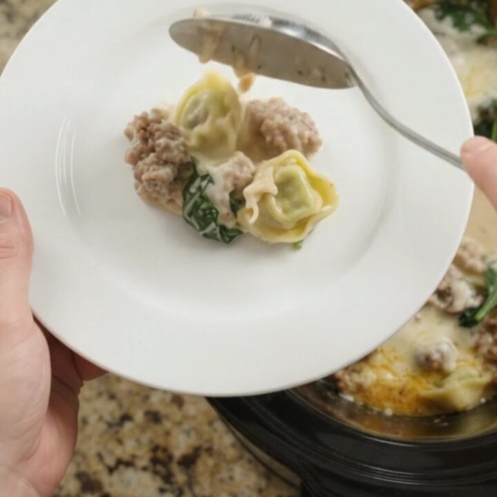 Creamy slow cooker tortellini with sausage and mushrooms in a black crockpot