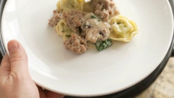Slow cooker filled with creamy provolone sausage spinach tortellini, bubbling and steaming