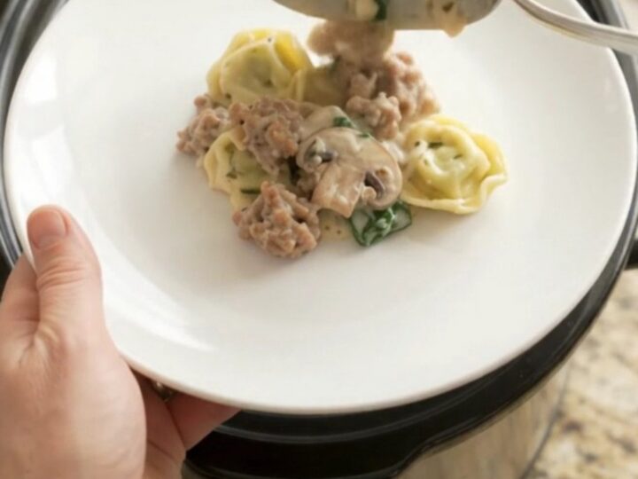 Slow cooker filled with creamy provolone sausage spinach tortellini, bubbling and steaming