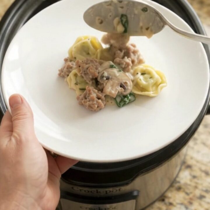 Slow cooker filled with creamy provolone sausage spinach tortellini, bubbling and steaming