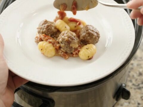 Bubbling slow cooker filled with meatballs, gnocchi, and melted provolone cheese