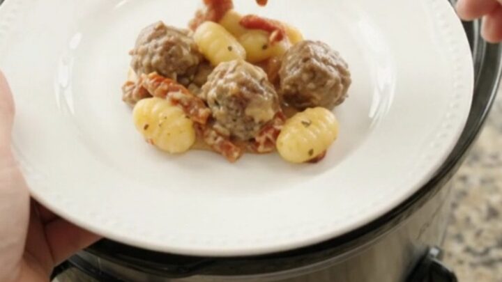 Bubbling slow cooker filled with meatballs, gnocchi, and melted provolone cheese