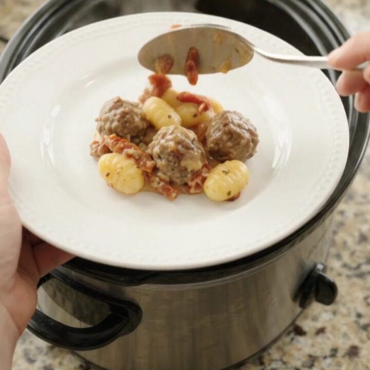 Bubbling slow cooker filled with meatballs, gnocchi, and melted provolone cheese