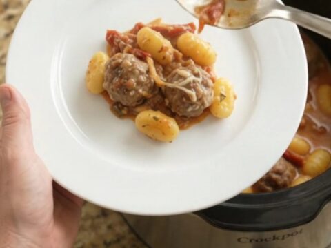 Slow cooker filled with meatballs, gnocchi, and melted mozzarella, creamy sauce bubbling