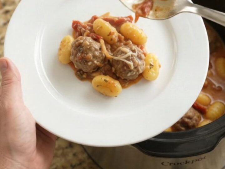 Slow cooker filled with meatballs, gnocchi, and melted mozzarella, creamy sauce bubbling