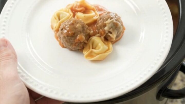 Slow cooker filled with meatballs, tortellini, and melted cheese, topped with mozzarella