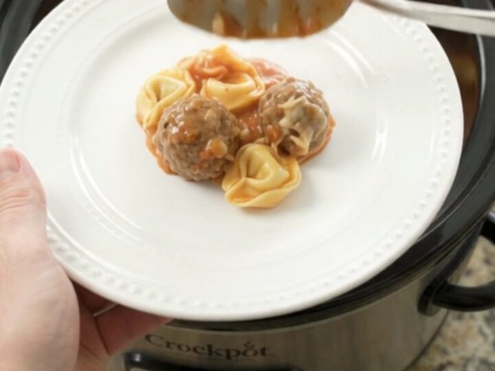 Slow cooker filled with meatballs, tortellini, and melted cheese, topped with mozzarella