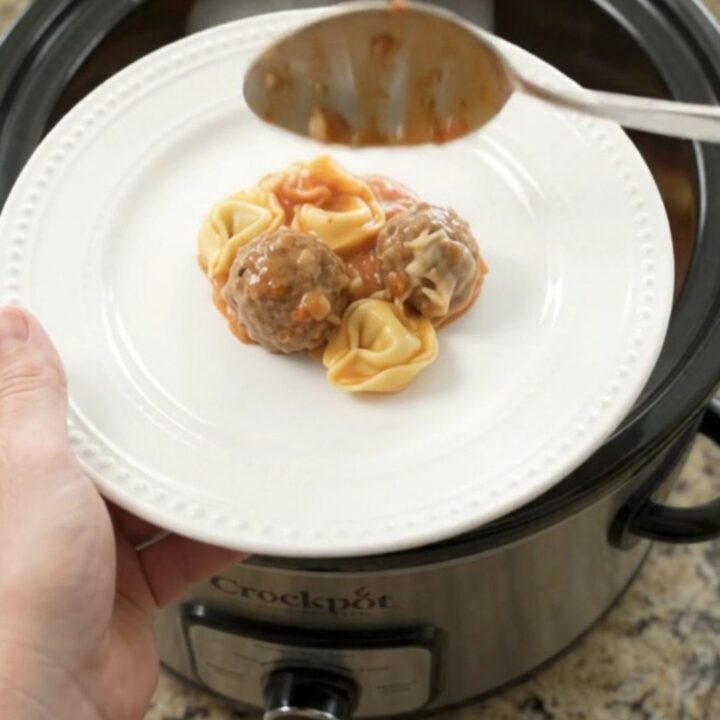 Slow cooker filled with meatballs, tortellini, and melted cheese, topped with mozzarella