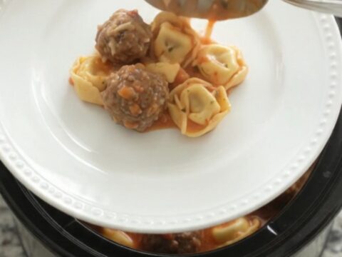 Slow cooker full of creamy tortellini and meatballs in tomato sauce with melted cheese