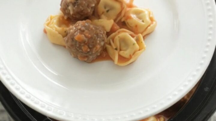 Slow cooker full of creamy tortellini and meatballs in tomato sauce with melted cheese