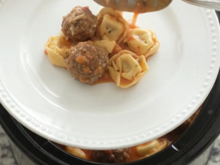 Slow cooker full of creamy tortellini and meatballs in tomato sauce with melted cheese