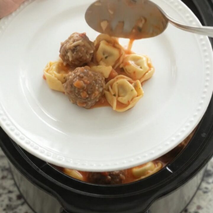 Slow cooker full of creamy tortellini and meatballs in tomato sauce with melted cheese