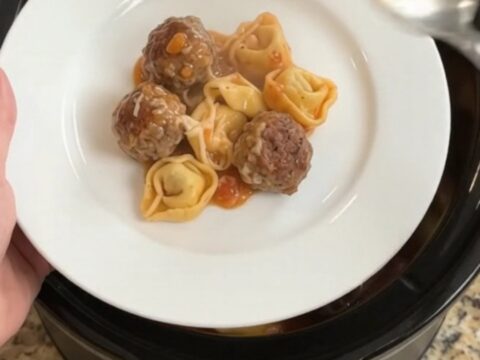 Slow cooker filled with meatballs, tortellini, and melted cheese