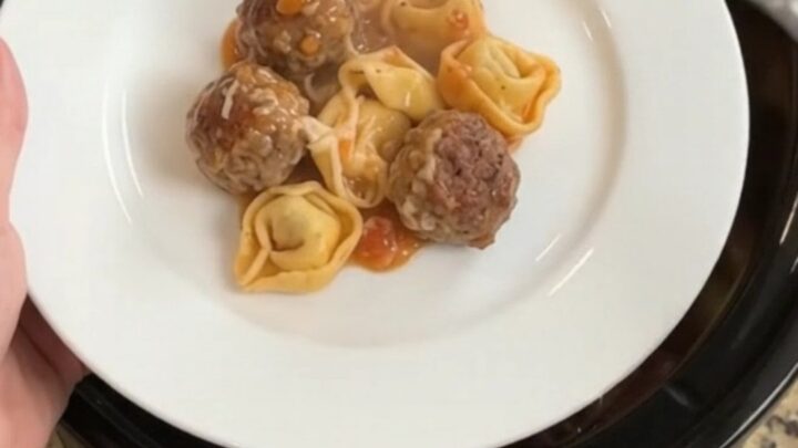 Slow cooker filled with meatballs, tortellini, and melted cheese