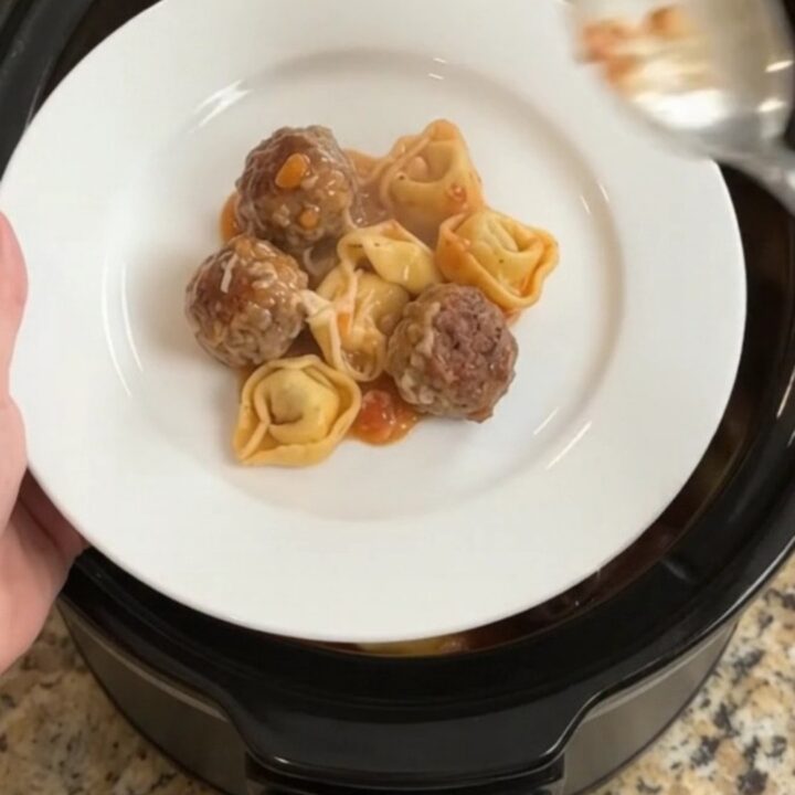 Slow cooker filled with meatballs, tortellini, and melted cheese