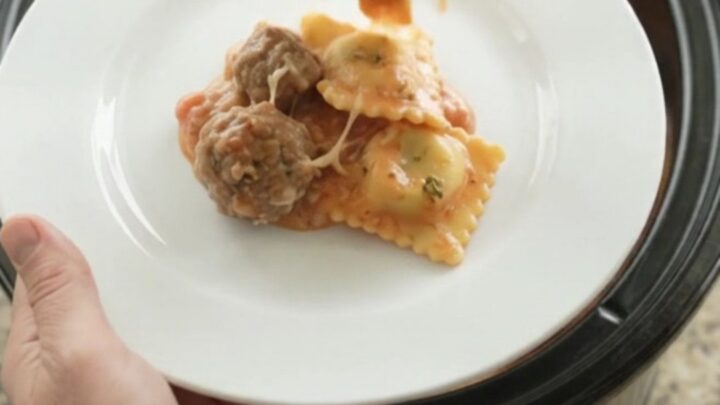 Slow cooker filled with meatballs, ravioli, and melted provolone cheese