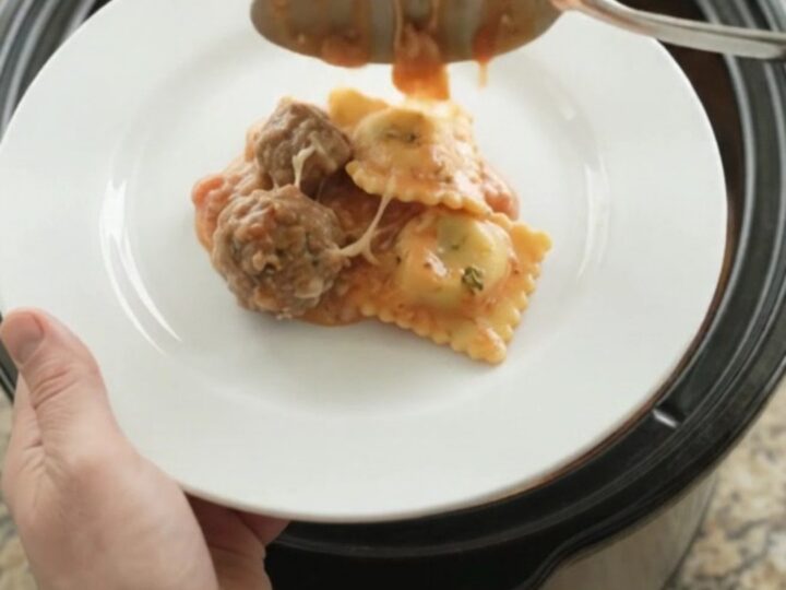 Slow cooker filled with meatballs, ravioli, and melted provolone cheese