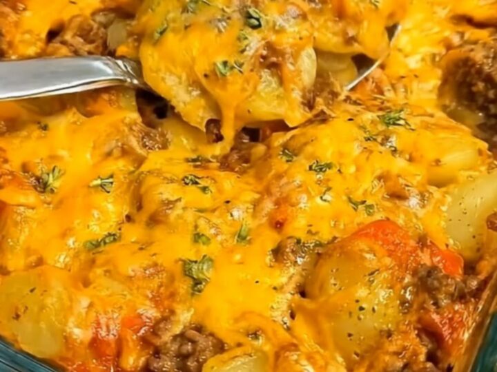 A metal serving spoon scooping a steaming portion of cheesy Hobo Casserole from a glass baking dish.