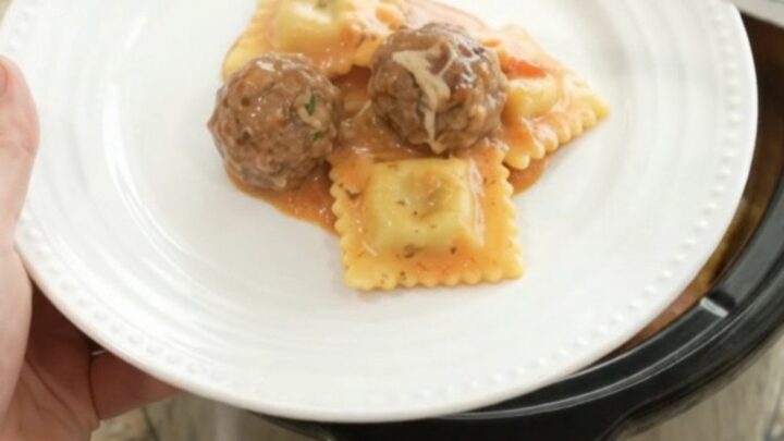 Slow cooker filled with creamy pasta and meatballs in pink vodka sauce, topped with melted fontina