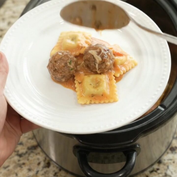 Slow cooker filled with creamy pasta and meatballs in pink vodka sauce, topped with melted fontina