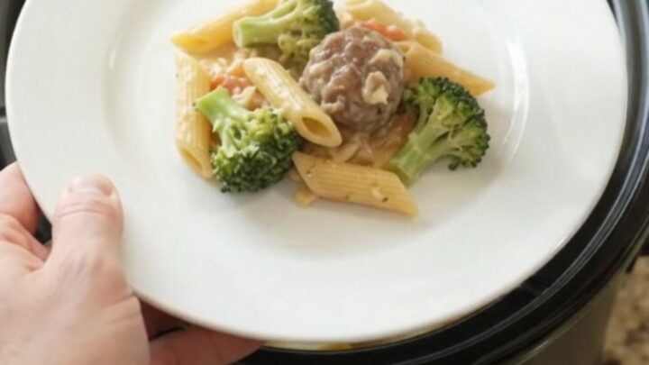 Crockpot full of creamy Alfredo penne with meatballs and melted cheese