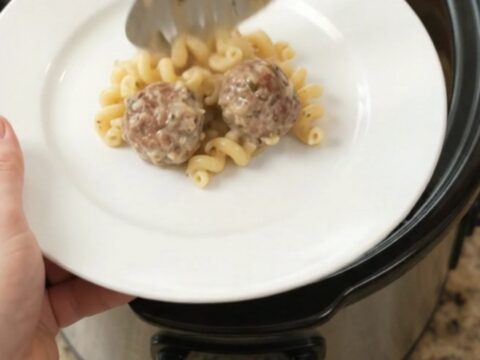 Bubbling slow cooker full of creamy cavatappi pasta and meatballs topped with melted cheese