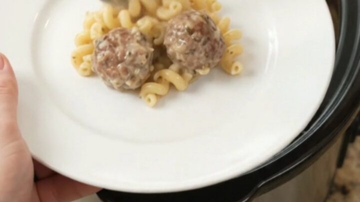 Bubbling slow cooker full of creamy cavatappi pasta and meatballs topped with melted cheese