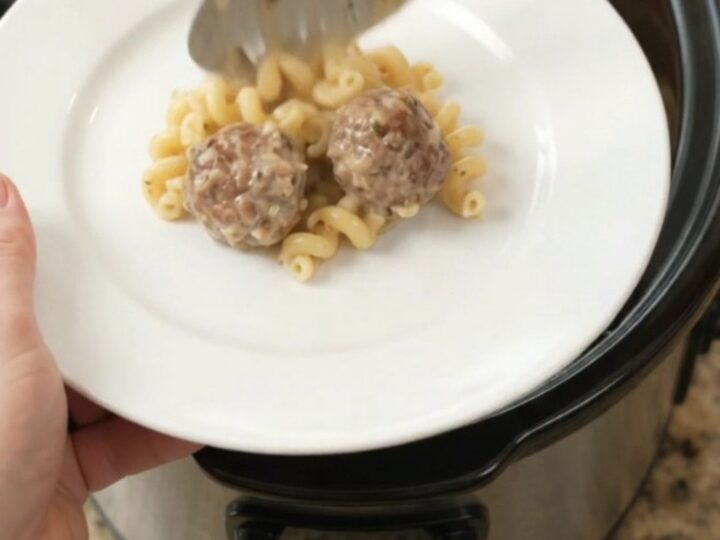 Bubbling slow cooker full of creamy cavatappi pasta and meatballs topped with melted cheese