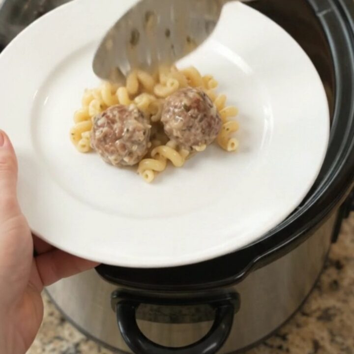 Bubbling slow cooker full of creamy cavatappi pasta and meatballs topped with melted cheese