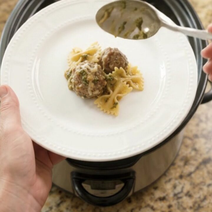 Slow cooker filled with creamy meatball pesto farfalle, topped with melted mozzarella.