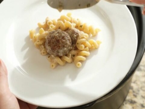 Slow cooker filled with creamy cavatappi pasta, meatballs, and melted provolone cheese, with a spoon lifting a cheesy scoop.