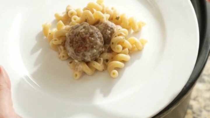 Slow cooker filled with creamy cavatappi pasta, meatballs, and melted provolone cheese, with a spoon lifting a cheesy scoop.