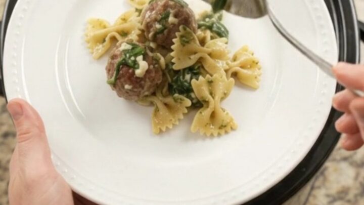 Bubbling Crockpot filled with meatballs, farfalle, spinach, and melted provolone cheese