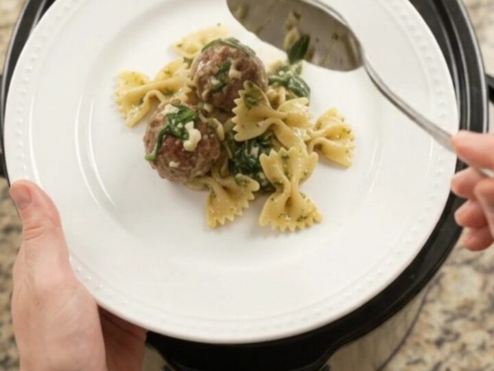 Bubbling Crockpot filled with meatballs, farfalle, spinach, and melted provolone cheese