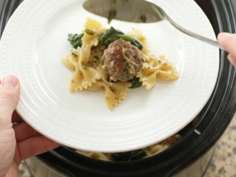 Slow cooker filled with cheesy meatball pesto farfalle, bubbling and golden