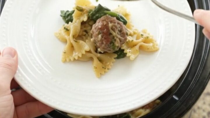 Slow cooker filled with cheesy meatball pesto farfalle, bubbling and golden
