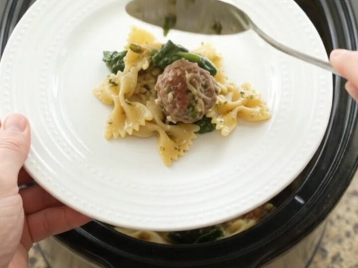 Slow cooker filled with cheesy meatball pesto farfalle, bubbling and golden