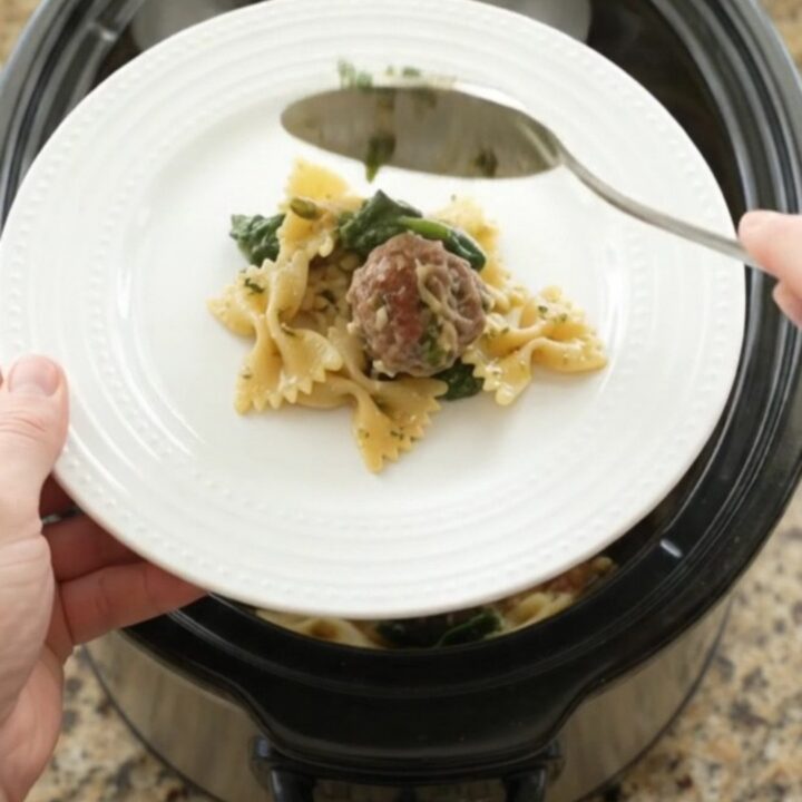 Slow cooker filled with cheesy meatball pesto farfalle, bubbling and golden