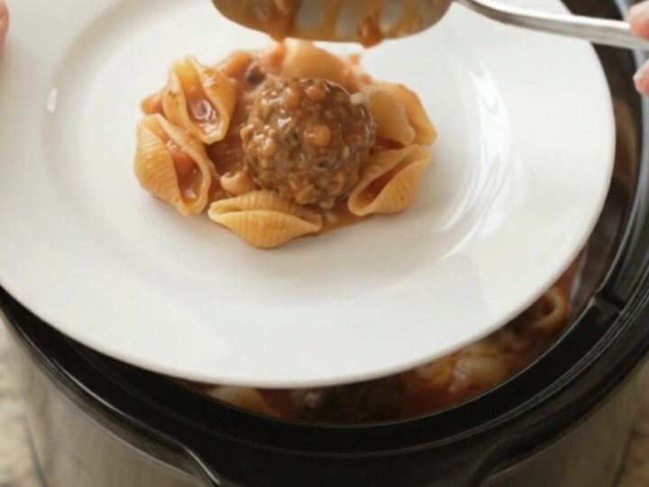 Slow cooker filled with meatballs, pasta shells, and red pepper sauce topped with ricotta and provolone.