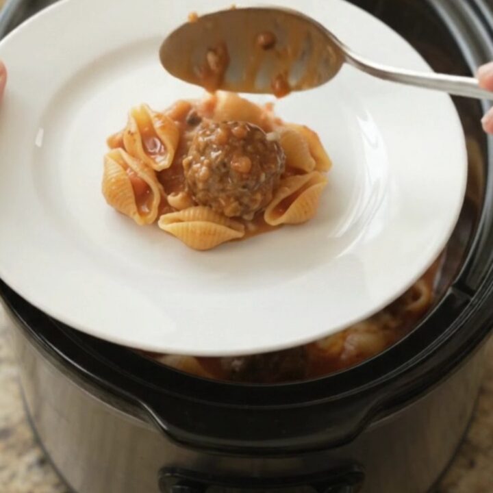 Slow cooker filled with meatballs, pasta shells, and red pepper sauce topped with ricotta and provolone.