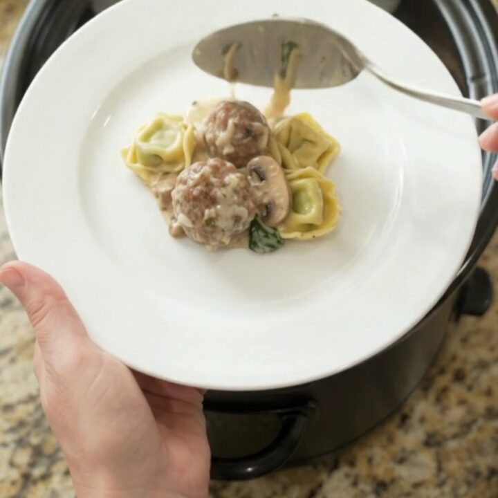 Slow cooker filled with cheesy meatball tortellini, bubbling with melted mozzarella and cream cheese sauce.