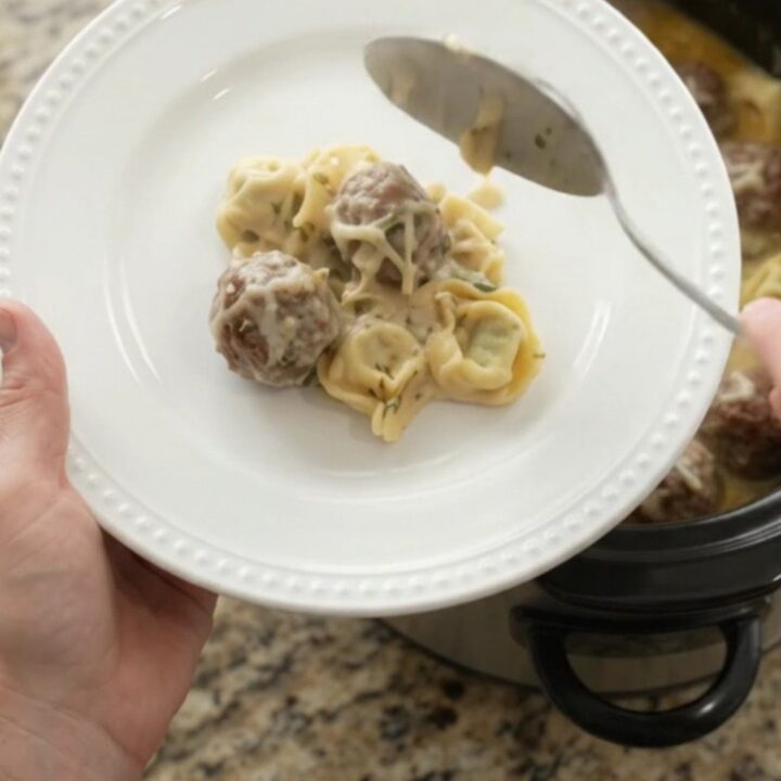 Crockpot filled with creamy Boursin meatball tortellini, topped with melted fontina