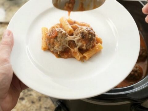 Slow cooker filled with bubbling Parmesan meatball baked ziti, cheese melted and golden