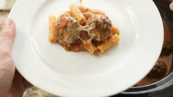 Slow cooker filled with bubbling Parmesan meatball baked ziti, cheese melted and golden