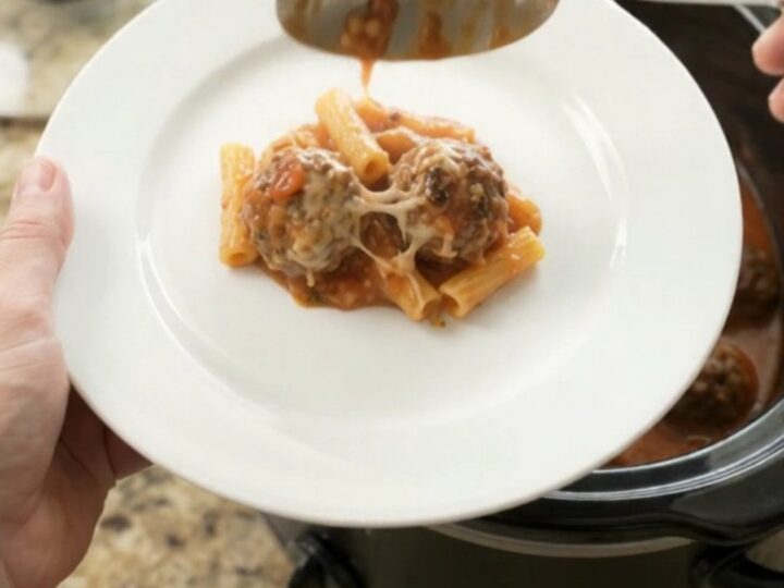Slow cooker filled with bubbling Parmesan meatball baked ziti, cheese melted and golden