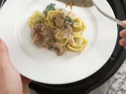 A slow cooker filled with bubbling Parmesan meatball spinach tortellini in creamy Alfredo sauce