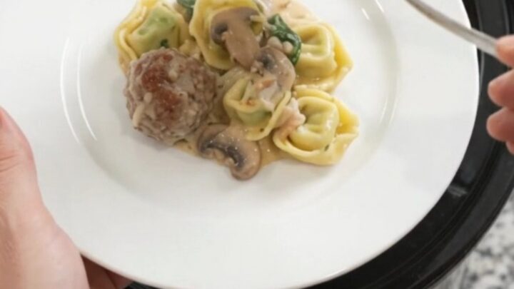 A slow cooker filled with bubbling Parmesan meatball spinach tortellini in creamy Alfredo sauce