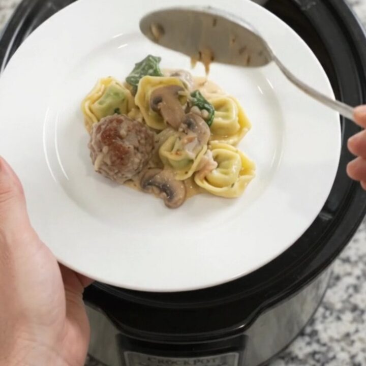 A slow cooker filled with bubbling Parmesan meatball spinach tortellini in creamy Alfredo sauce