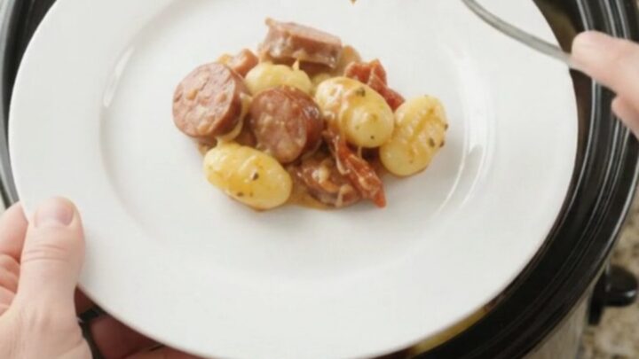 Slow cooker filled with creamy kielbasa Tuscan gnocchi, topped with melted provolone and ricotta
